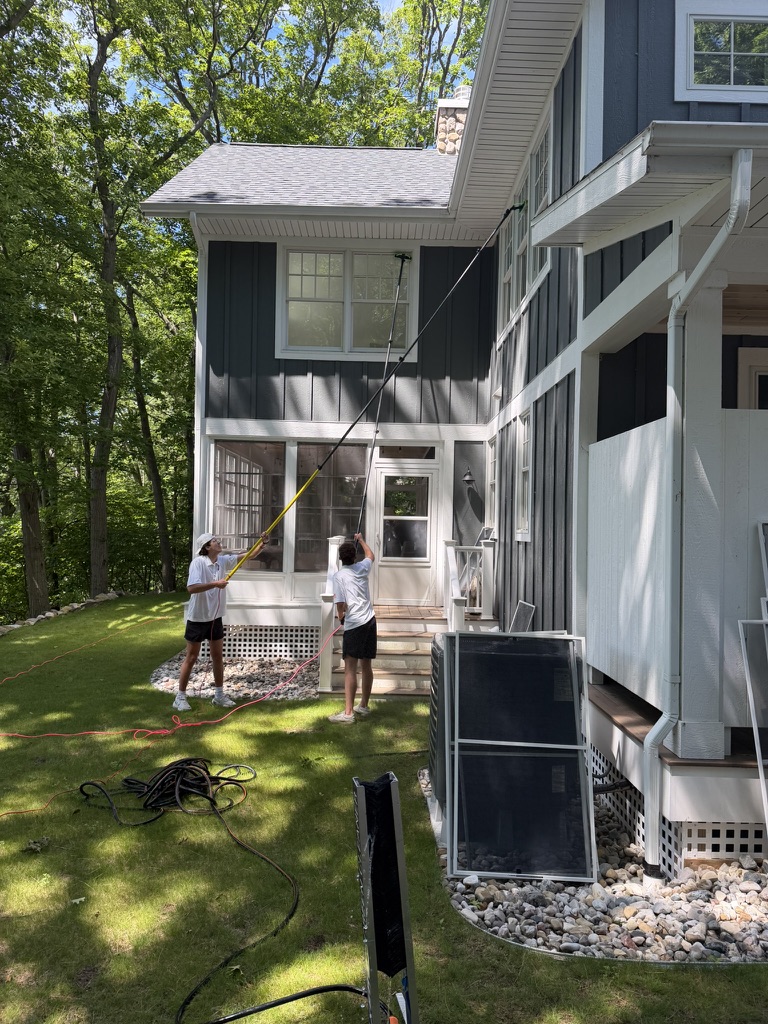 Two team members washing second-story windows on a blue home
